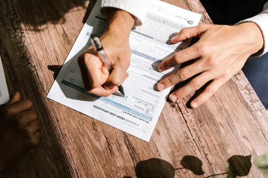 Mãos preenchendo um formulário de solicitação de crédito pessoal sobre uma mesa de madeira.