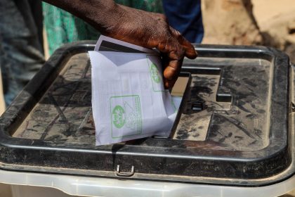 Mão colocando uma cédula de papel em uma urna eleitoral transparente ao ar livre