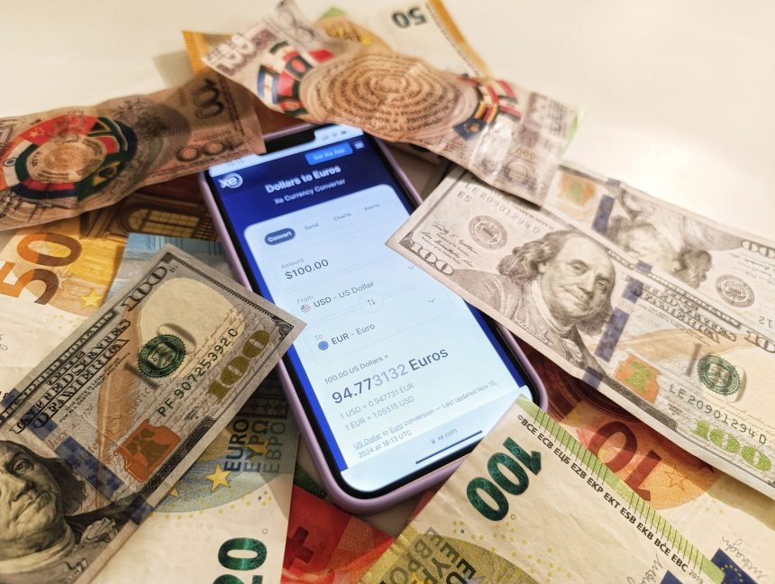Smartphone exibindo um conversor de moedas, cercado por cédulas de dólar e euro.