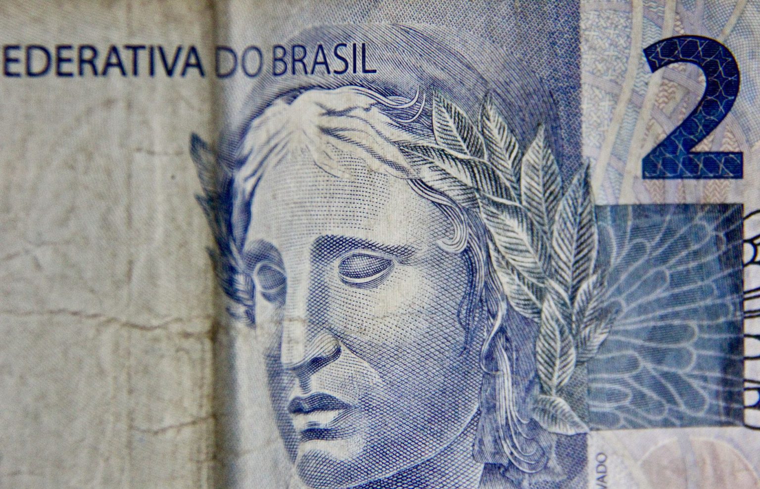 Close-up de uma cédula brasileira de dois reais, destacando seus elementos gráficos.